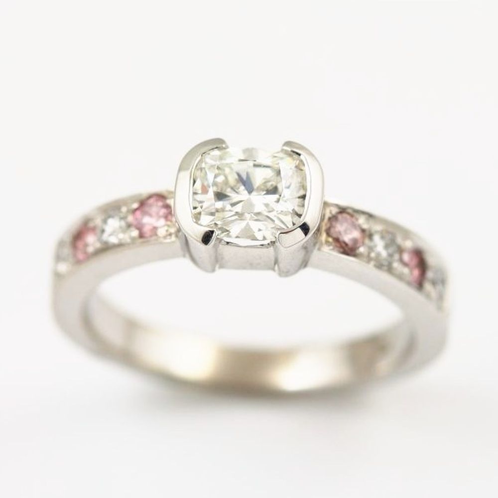 A cushion-cut diamond in a white gold half-bezel, with pink and white diamonds set along the band