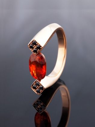 A rose gold ring standing on its reflection, an orange garnet between two squares of black diamonds