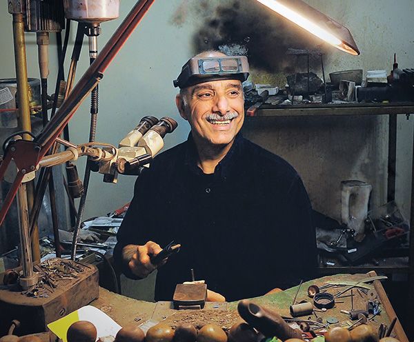 Eytan Aharoni smiling at his jeweller's bench, magnifying visor on his head
