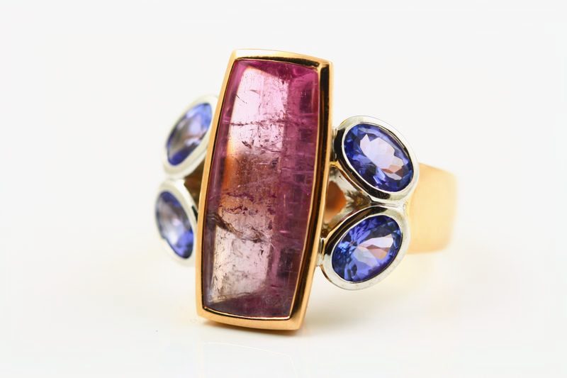 A yellow gold ring with a rectangular pink tourmaline between two oval blue tanzanites