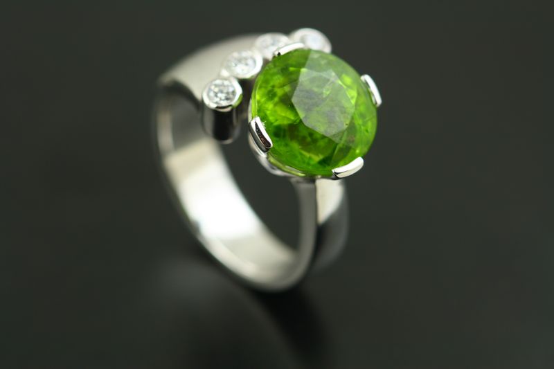 A white gold open ring with a round Peridot and small diamonds on the shoulders