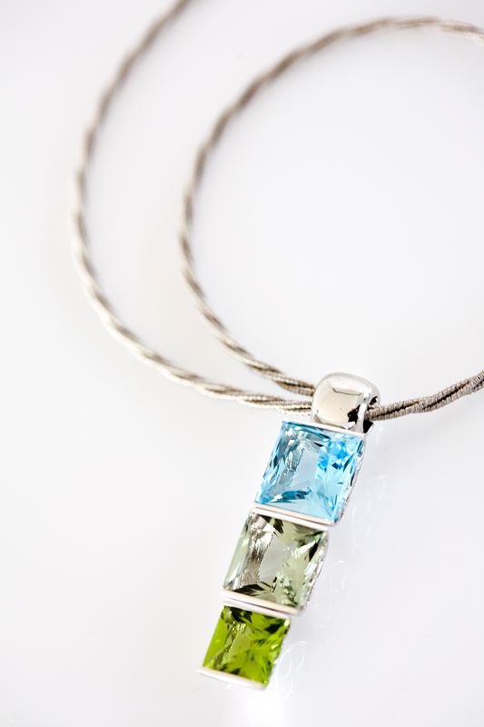 A pendant of three square stones in blue, pale green and green stacked on a twisted cable