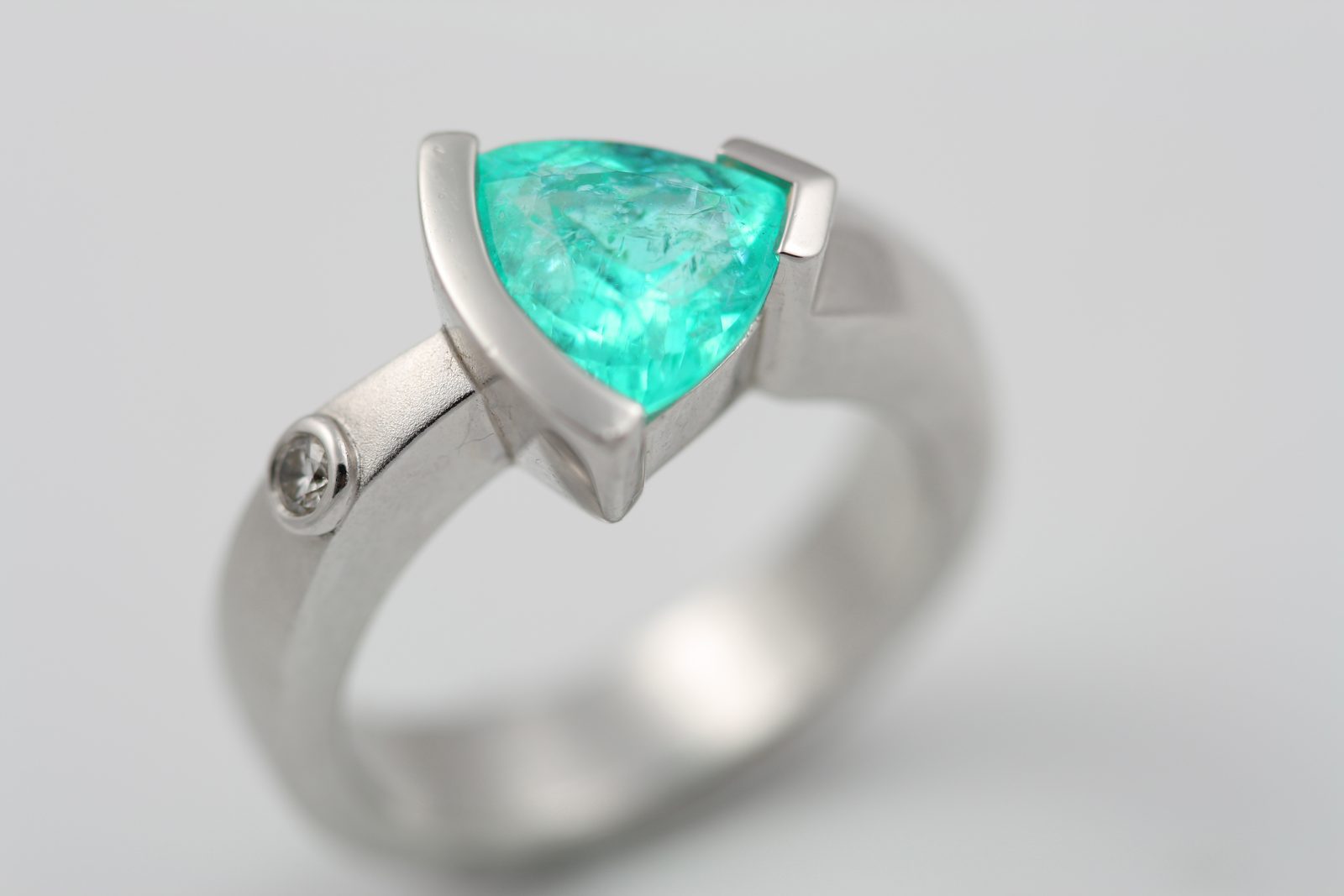 A minimal white metal ring holding a green-blue trillion-cut tourmaline