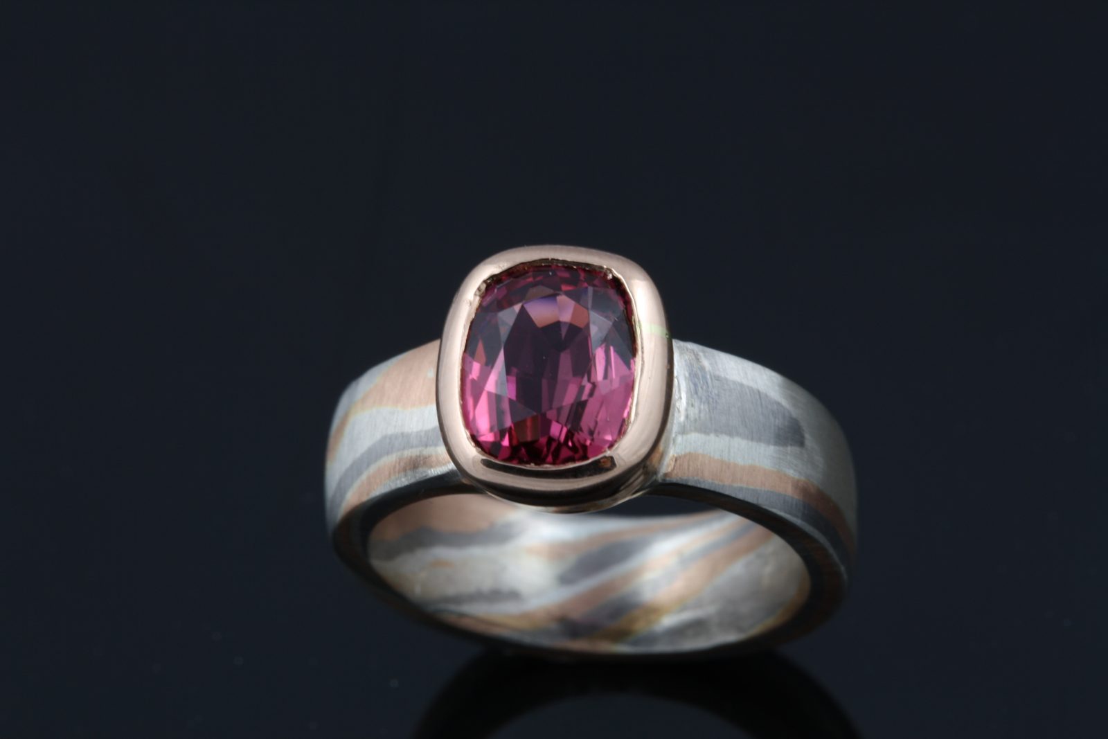 A cushion-cut pink tourmaline set on a Mokume Gane band, on black
