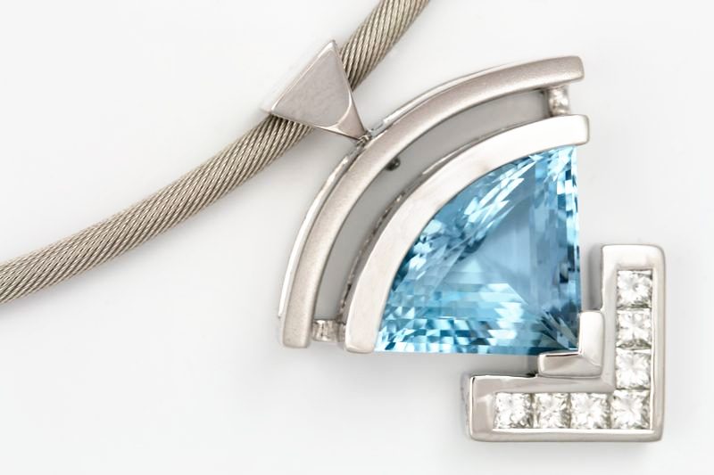 A fan-shaped white gold pendant with a triangular aquamarine and a line of small diamonds, on a cable