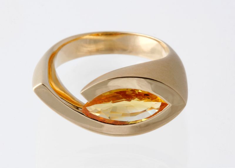 A swirling yellow gold ring holding a marquise-cut golden imperial topaz