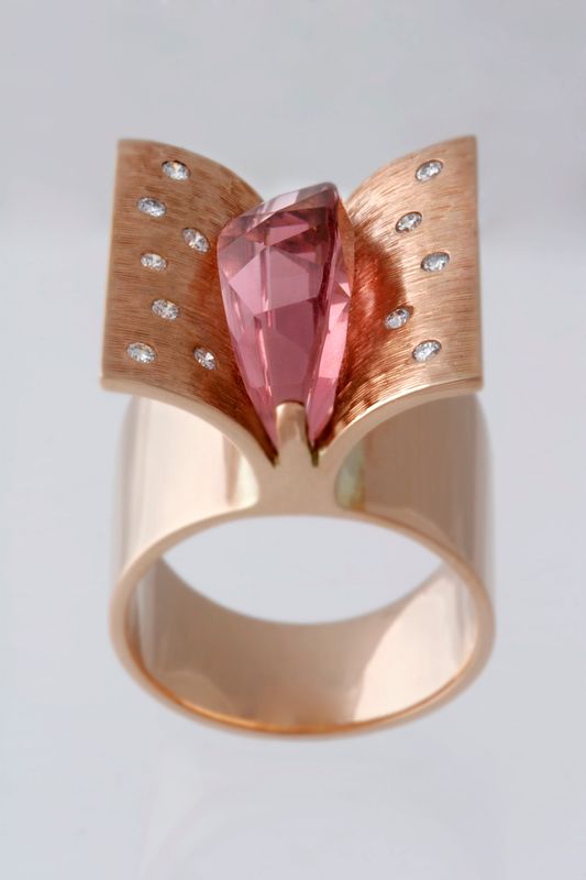 A wide rose gold ring with two flared wings scattered with diamonds around a pink tourmaline