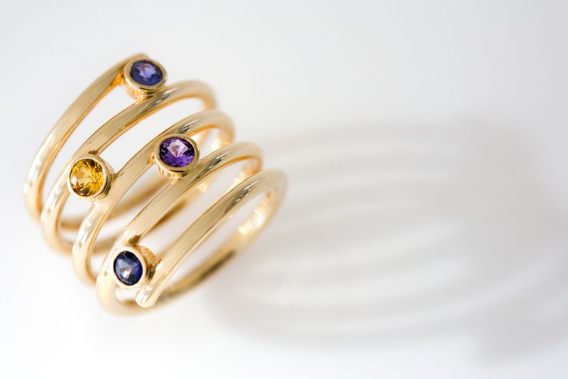A triple-coil yellow gold ring with small violet and yellow stones