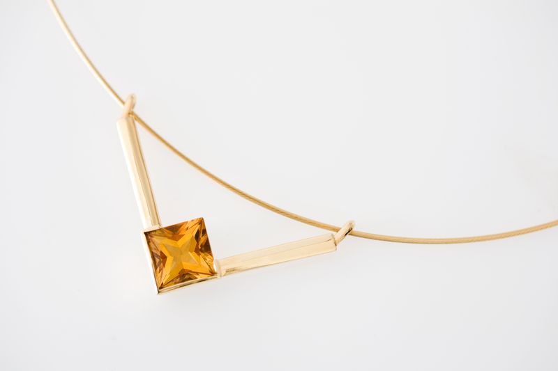 A gold V-form necklace with a square golden citrine at its point