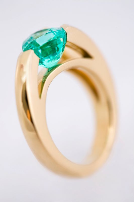 A sculpted yellow gold ring holding a bright teal cushion-cut tourmaline