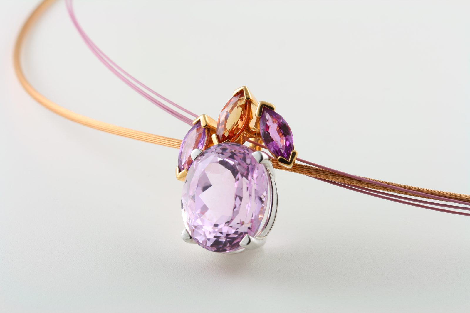 A lilac oval kunzite pendant topped with small pink and orange stones on a fine cable