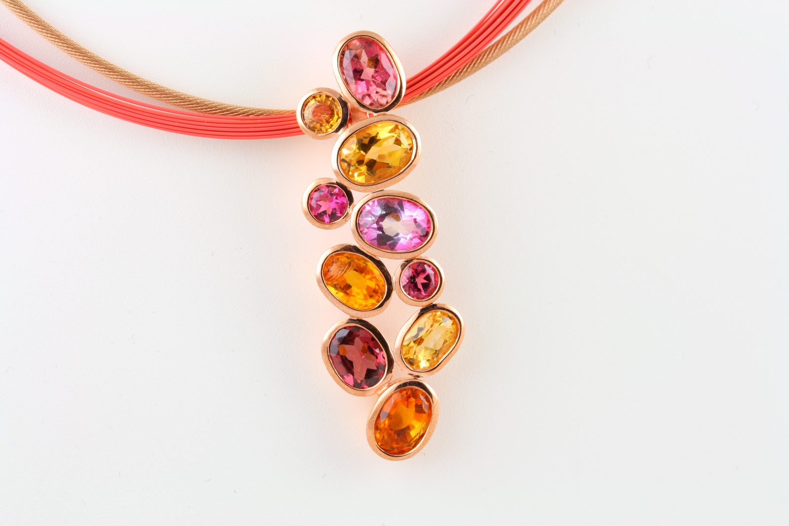 A cascade of oval orange, yellow and pink stones on a fine red cord