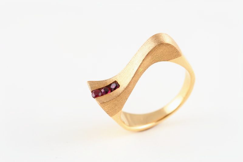 A rose gold ring with a wave-shaped shoulder set with three small rubies