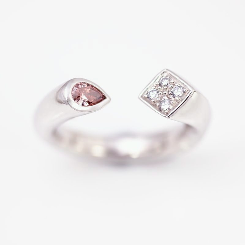 An open platinum ring ending in a pear-shaped pink diamond and a square set with blue diamonds