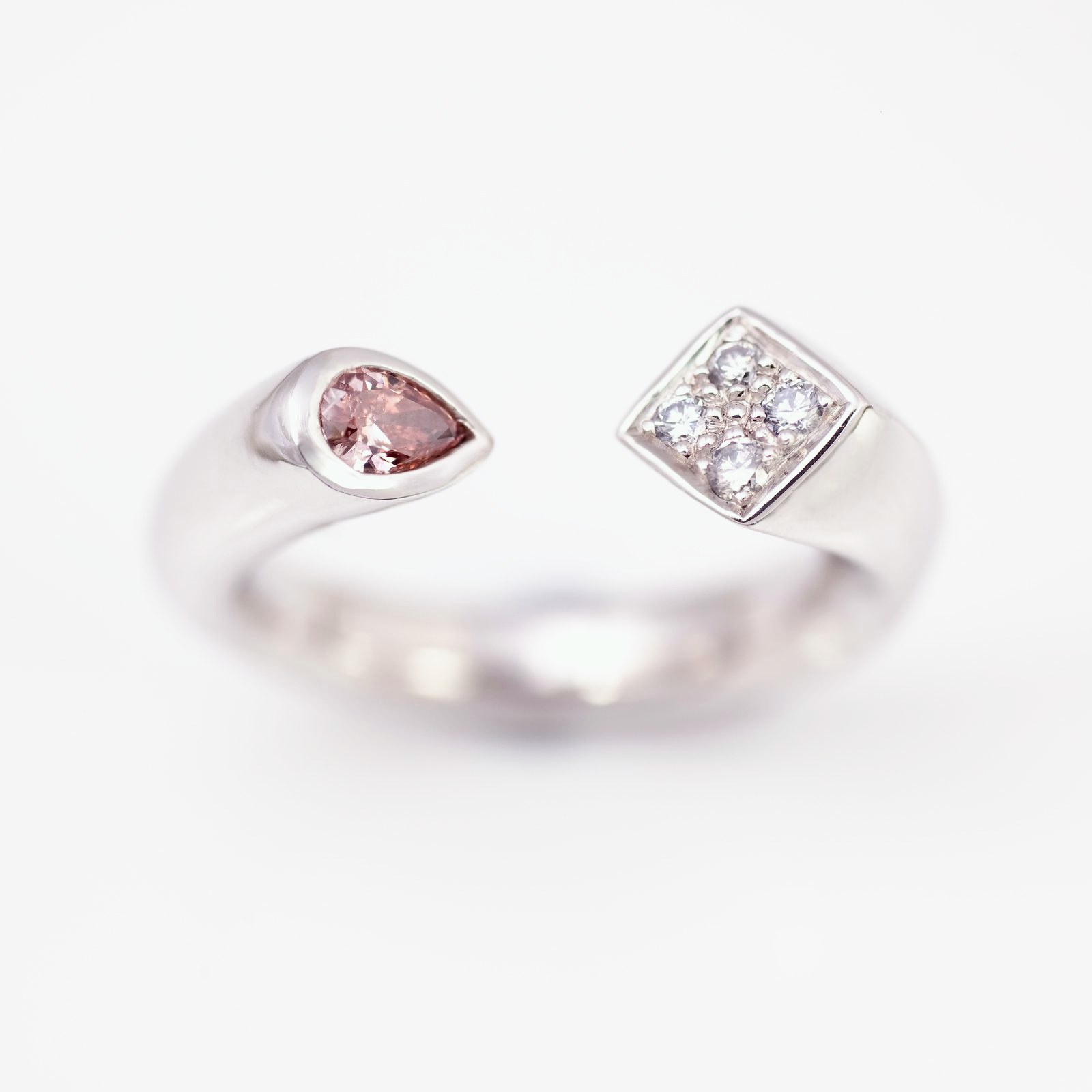 An open platinum ring ending in a pear-shaped pink diamond and a square set with blue diamonds