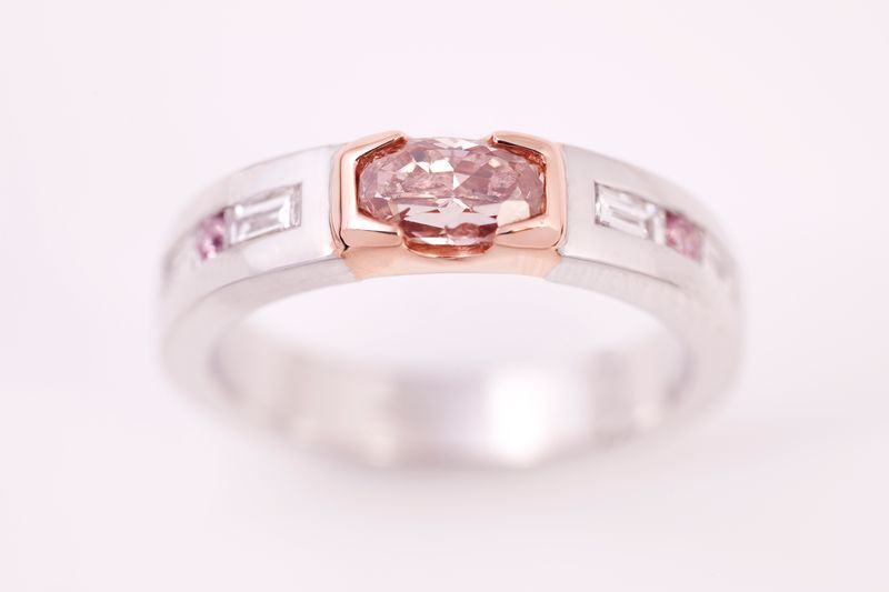 A white gold band with a rose gold centre holding an oval pink sapphire between baguette diamonds