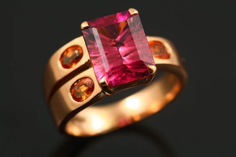 A rose gold ring with an emerald-cut pink tourmaline and two small orange sapphires