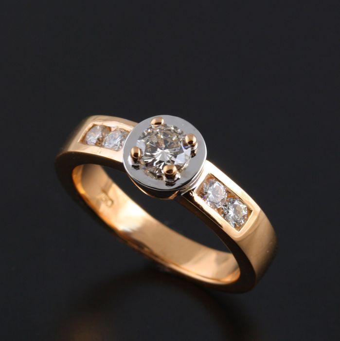 Diamond engagement ring: a diamond with rose gold claws on a round base of 18 karat white gold, with two diamonds on either side of it in an 18 karat rose gold band