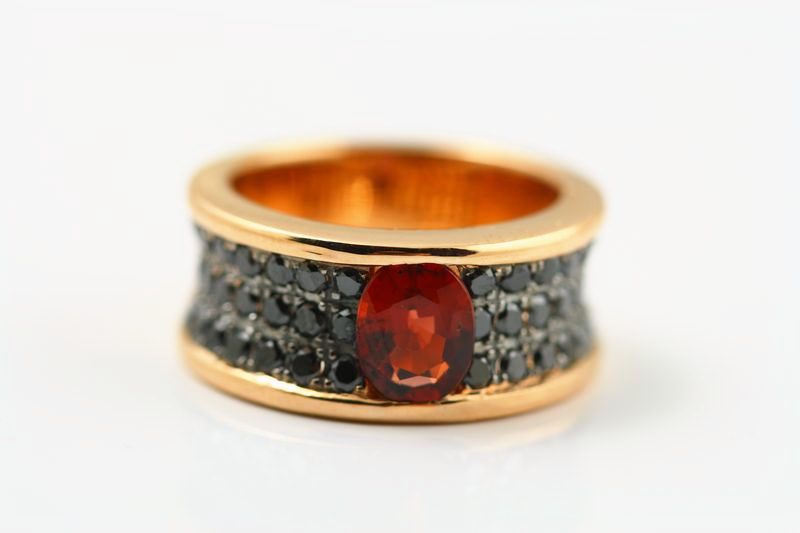 A rose gold band with an oval red garnet on a field of black diamonds