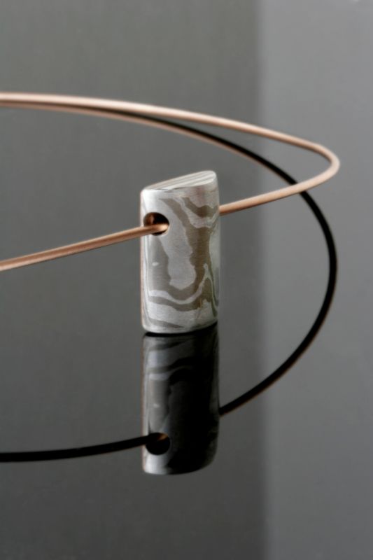 A small Mokume Gane cylinder pendant on a fine wire, on black