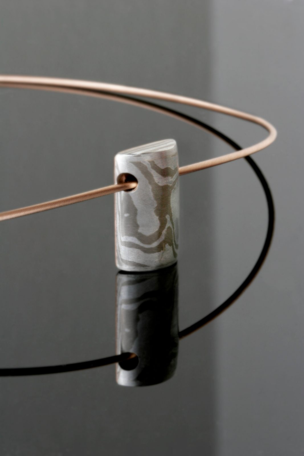 A small Mokume Gane cylinder pendant on a fine wire, on black