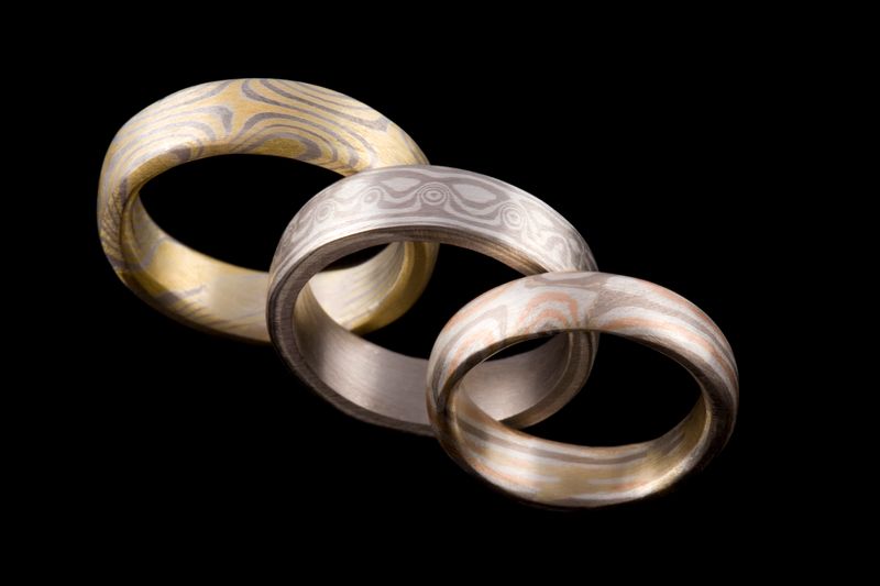 Three Mokume Gane wedding bands of different widths, each with a different grain, on black