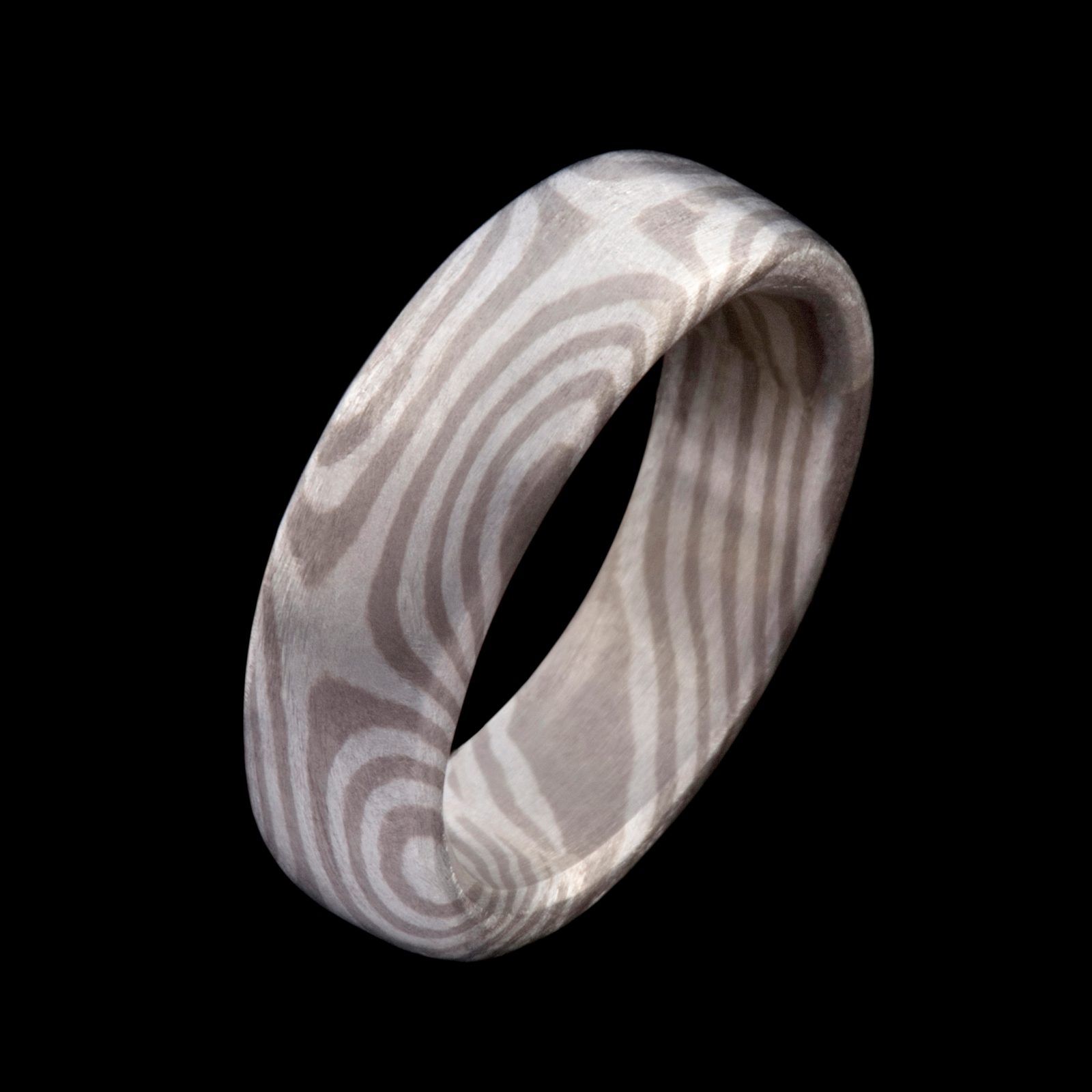 A wide Mokume Gane band, its surface patterned with pale wood-grain rings, on black