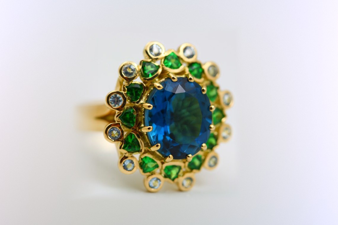 London Blue Topaz halo ring: a London Blue Topaz with Tsavorites and Aquamarines in 18 karat yellow gold