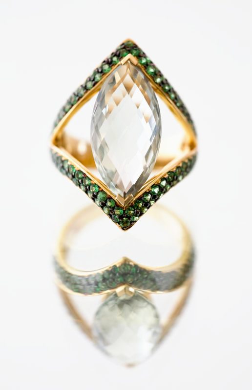 A marquise pale green stone in a diamond-shaped frame of tiny green stones, standing on its reflection