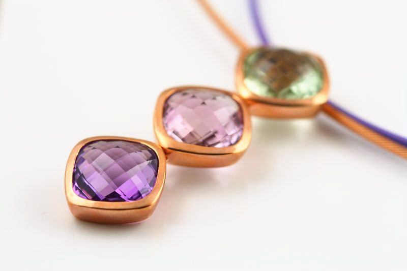 Two checker-cut amethyst cushions and a green tourmaline on a violet cord