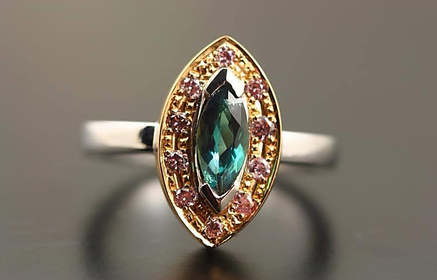 A marquise alexandrite in a white gold setting, framed by a yellow gold halo of small pink stones, on a white gold band